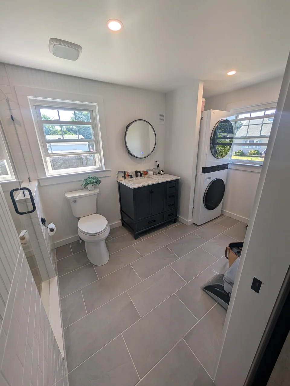 Bathroom showing a dark vanity, tiled floor, and stacked laundry.