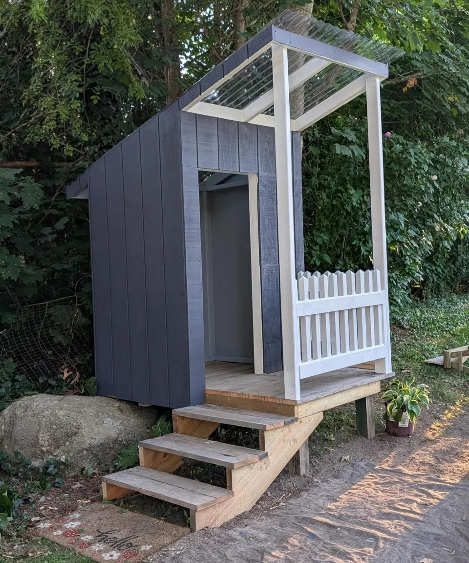 Blue-gray playhouse with a small porch, steps, and a clear roof.